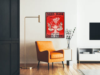 Vintage-mainosjuliste Paris–Dijon, lelut ja uutuudet, kehystetty olohuoneessa oranssin nojatuolin ja lattiavalaisimen vierellä.