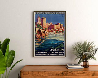 Vintage-matkailujuliste – Avignon, romaninen ja keskiaikainen Ranska, kehystettynä puupöydän yläpuolella kasvien välissä.