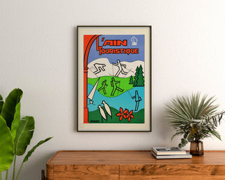 Vintagematkailujuliste – L’Ain touristique, kehystetty puukommodin yläpuolelle kasvien väliin.