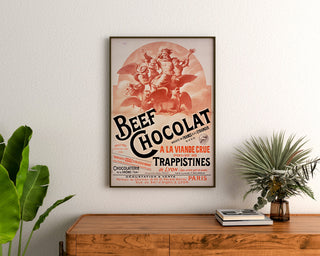 Vintage-juliste Beef Chocolat, Drômen suklaatehdas, kehystettynä puupöydän yläpuolella kasvien välissä.