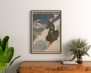 Vintagetyylinen Chamonix-juliste, winter sports PLM, kehystettynä puukomodin yläpuolella kasvien ympäröimänä.