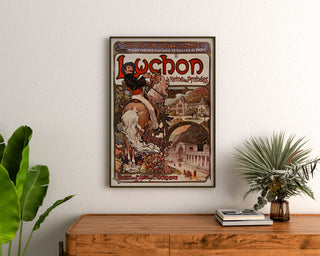 Vintage-juliste Luchon, Pyreneiden kuningatar, kehystetty puupöydän yläpuolelle kasvien väliin.