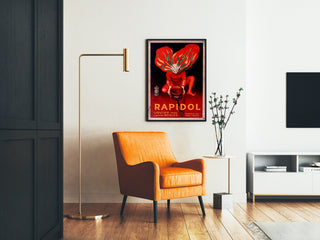 Vintage-juliste Rapidol, kehystetty olohuoneessa oranssin nojatuolin ja lattiavalaisimen vieressä.