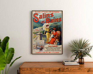 Vintage-juliste Salins-les-Bains (Jura), kehystetty puupöydän yläpuolelle, viherkasvien välissä.
