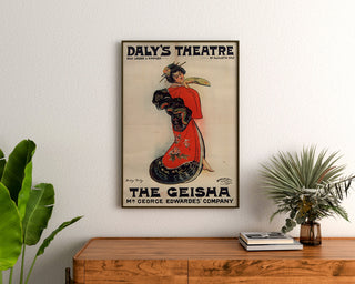 Vintage-juliste The Geisha, Daly’s Theatre, kehystettynä puupöydän yläpuolella kasvien välissä.